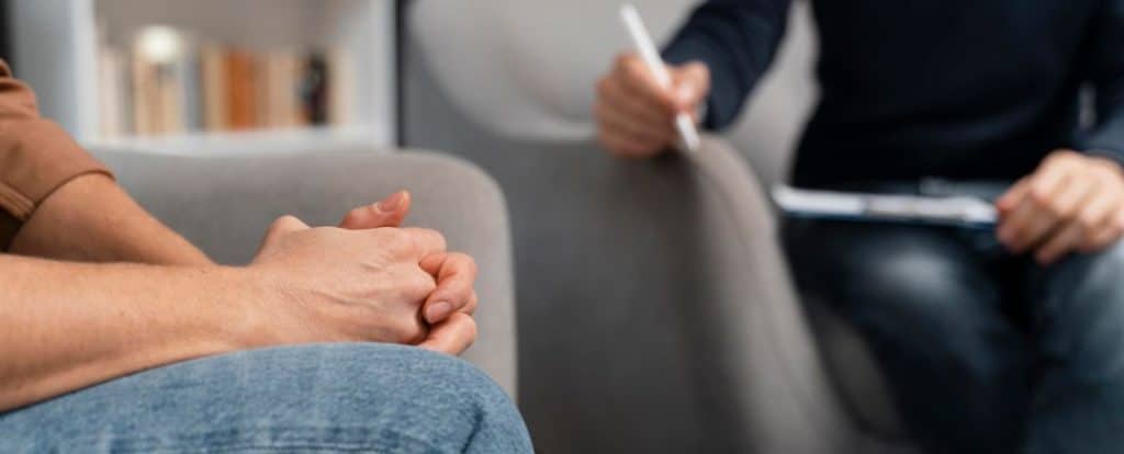 טיפול CBT מצולם בעוד שהמטפל והמטופל שניהם מצולמים בפלג הגוף התחתון. המטופל משלב ידיים והמטפל רושם במחברת. 