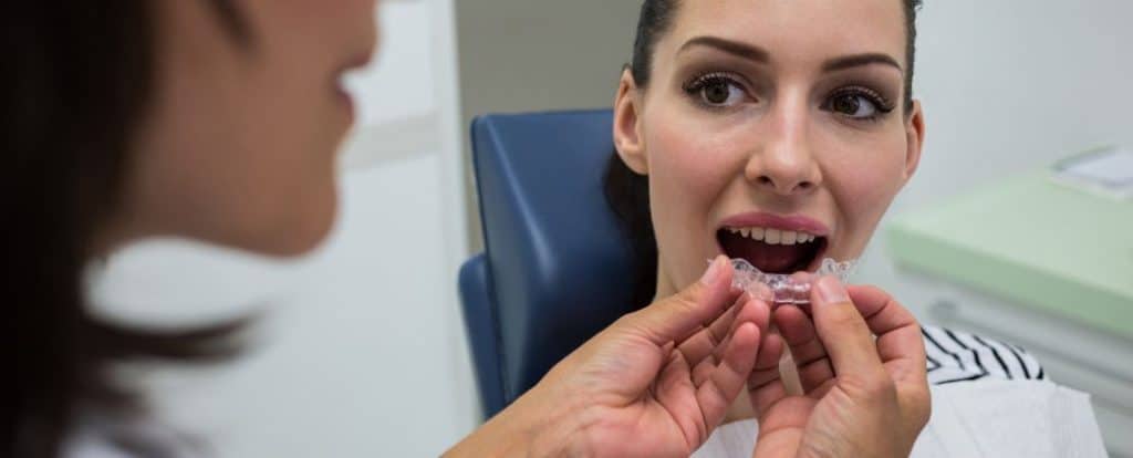 אשת צוות רפואי מראה למטופלת פלטה שקופה ומסבירה למה יותר מבוגרים בוחרים היום ביישור שיניים שקוף?
