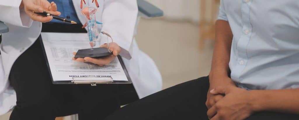 ניתן לראות פלגי גוף תחתונים של רופא ומטופל והמטופל מחזיק את מפשעתו בעת קבלת בשורות לגבי סרטן בדרכי השתן
